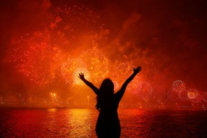 A woman celebrates the New Year as she watches fireworks exploding above Copacabana beach in Rio de Janeiro